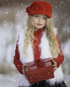 niña rubia con gorro bajo la nieve sosteniendo un regalo de navidad