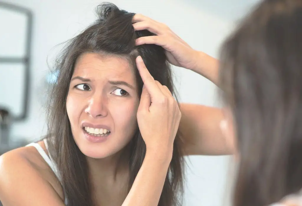 Mujer frente al espejo mirando la caspa de su cabello