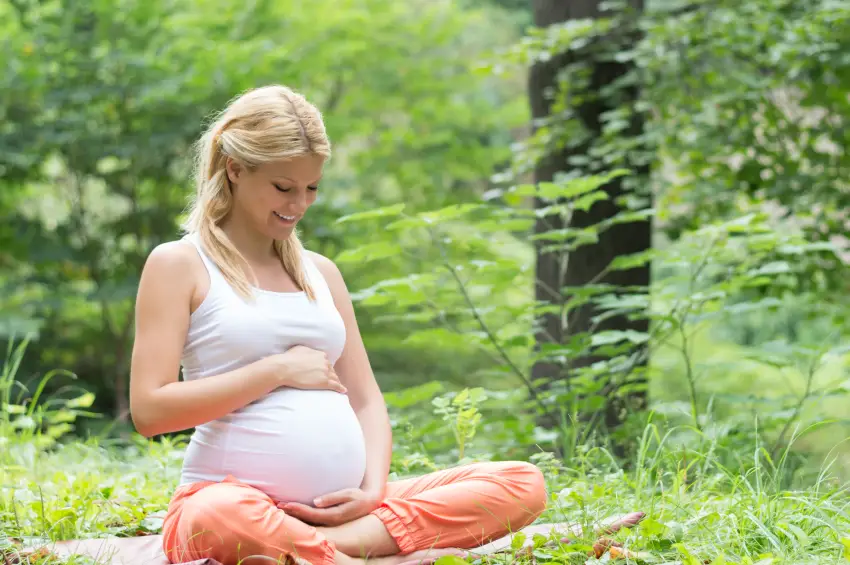 Mujer embazarada sentada en un parque, con una postura de yoga