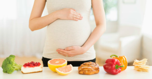 vitaminas para embarazadas Mujer embarazada frente a una mesa de alimentos sanos
