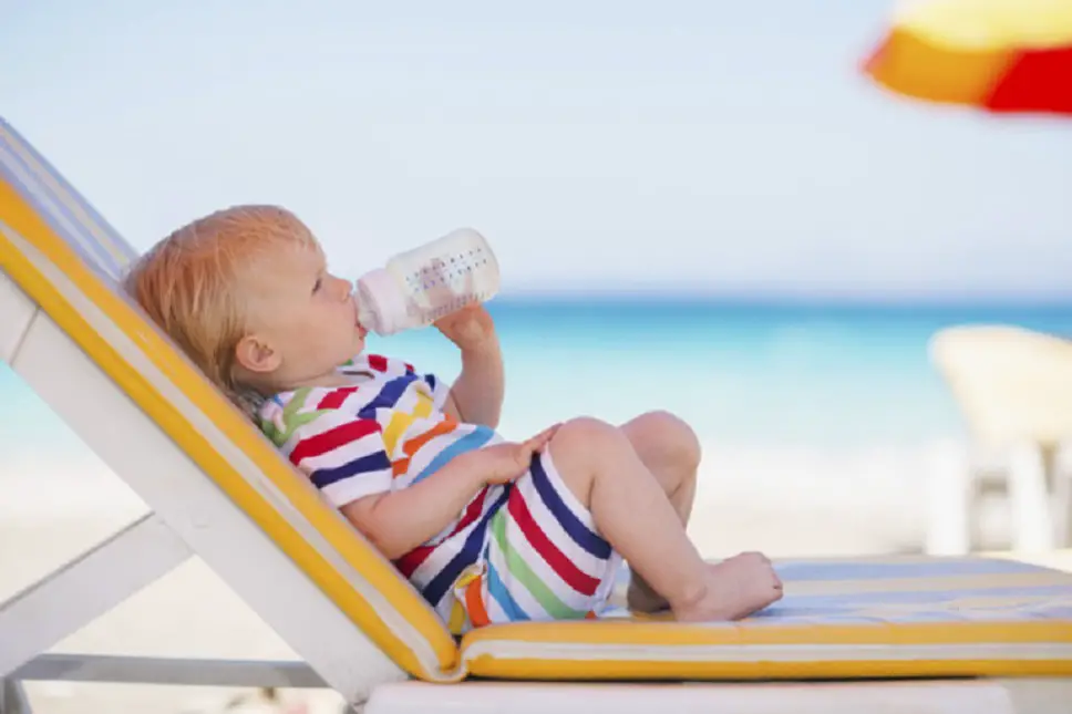 Bebé en la playa debajo de una sombrilla tomando leche